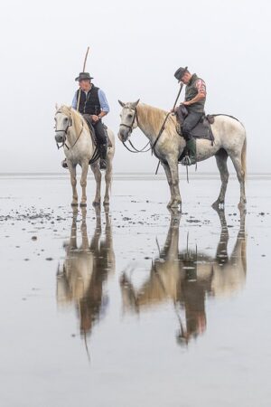 Photo en tirage limité. Série chevaux de camargue de Michèle Gabet Photographie. 2 gardians et leurs chevaux en bord de mer se reflettent dans l'eau