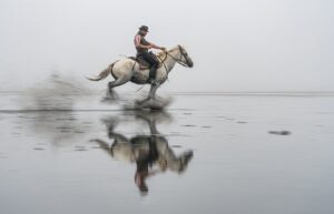 Photo en tirage limité. Série chevaux de camargue de Michèle Gabet Photographie. gardian et son cheval au grand galop dans l'eau. reflet dans l'eau