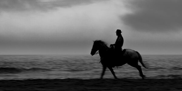 Photo en tirage limité en noir et blanc. Série chevaux de camargue de Michèle Gabet Photographie. cheval et son cavalier au galop sur la plage